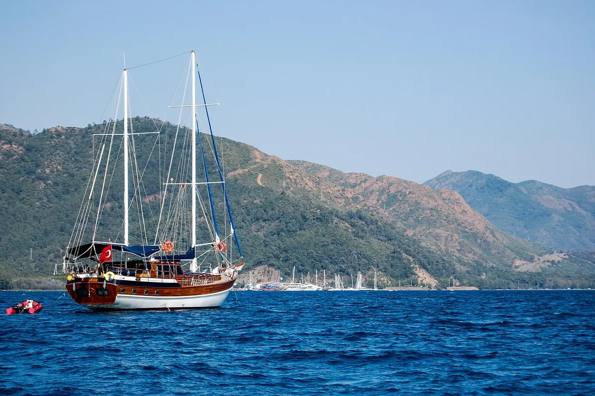 A gulet sailing past green hills