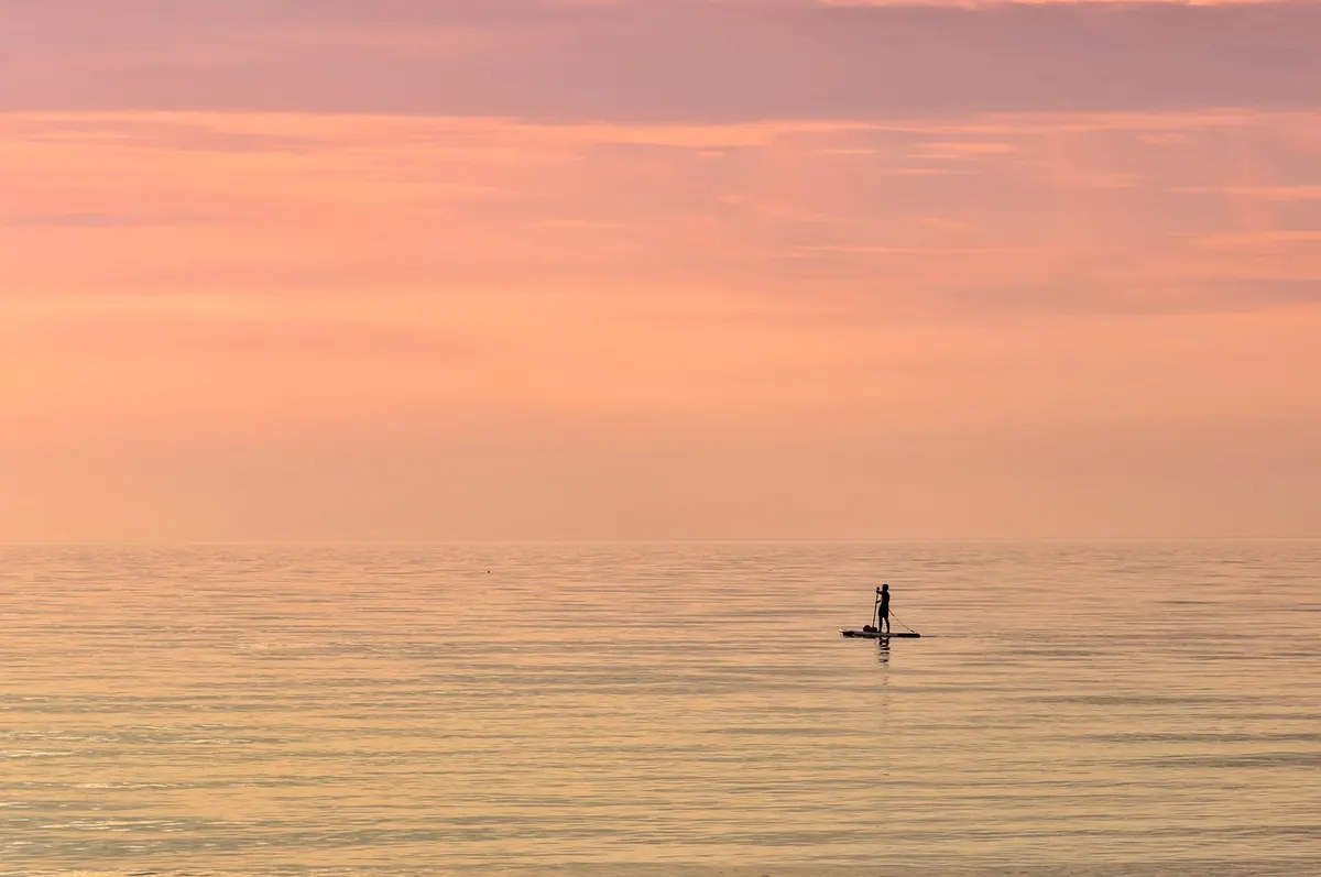 A paddleboarder on a calm sea at sunset